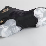 Chaussure de boxe noir et or posée sur le côté, débord de semelle claire