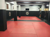 Salle de MMA équipée de tatamis vinyle lisse rouges, protections murales et de poteaux noires, sacs de frappe suspendus