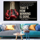 Tableau gants de boxe rouges suspendus a un poteau de bois et citation en capitales creme, vue rapprochee de la toile