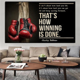 Tableau gants de boxe rouges suspendus a un poteau de bois et citation en capitales creme, affiche dans un salon