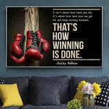 Tableau gants de boxe rouges suspendus a un poteau de bois et citation en capitales creme, accroche dans une entree